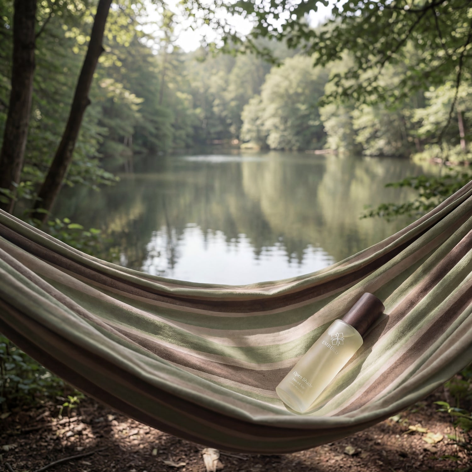 Open Shade pillow mist resting in a striped hammock, a still lake and green forest canopy beyond