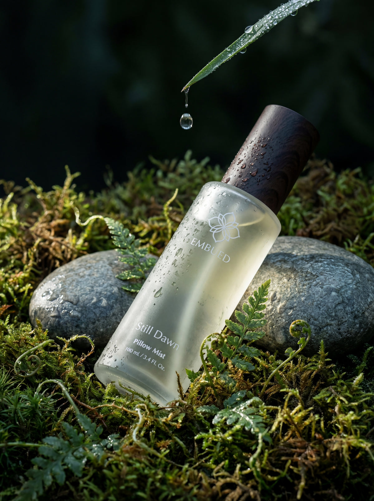 Still Dawn pillow mist on moss and stone, a drop of water falling from a leaf above the frosted bottle