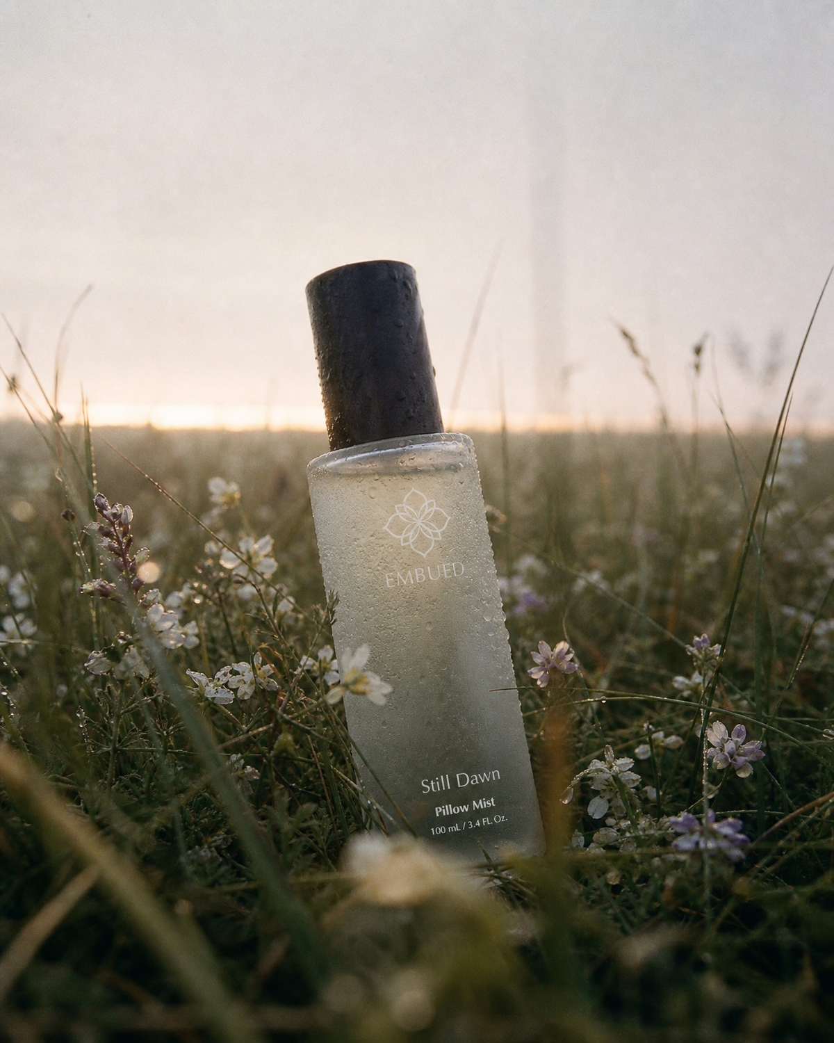 Embued Still Dawn ethanol-free pillow mist bottle standing in a wildflower meadow at golden hour